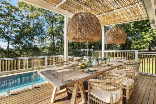 a wooden table and chairs on a deck with a pool at Meadows Estate in Bangalow