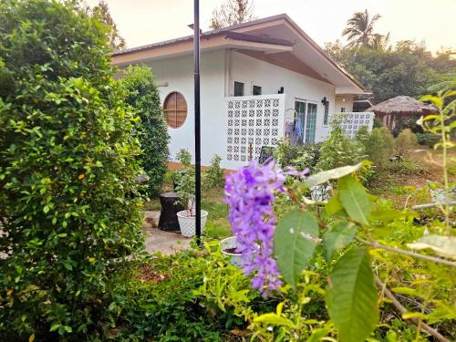 a garden with purple flowers in front of a house at Baan suan khun ta บ้านพักสวนคุณตา in Ko Chang