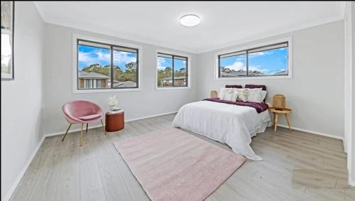 - une chambre blanche avec un lit et une chaise rose dans l'établissement Center of Rouse Hill house with fully fenced back yard, à Riverstone