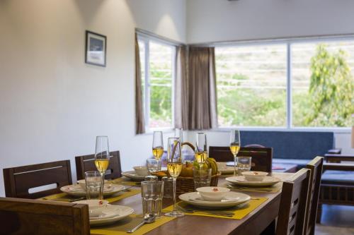a dining room with a table with glasses of wine at Alaya Stays Kodiyat 4-BHK Pet-Friendly Villa With Views of Sajjangarh Palace in Nāi