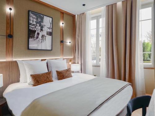 un grand lit blanc dans une pièce avec des fenêtres dans l'établissement Merveil - Signature Suite - Champs Elysees - Dulud I, à Neuilly-sur-Seine