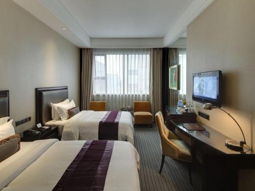 a hotel room with two beds and a desk and a television at New Century Manju Hotel Shanghai New International Expo Center in Shanghai