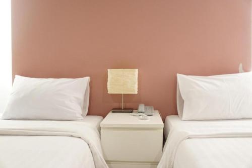 two beds with white pillows and a table with a lamp at The One Residence Hotel in Bangkok