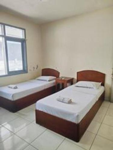 two beds in a room with a window at Alexander Hotel Tegal in Tegal