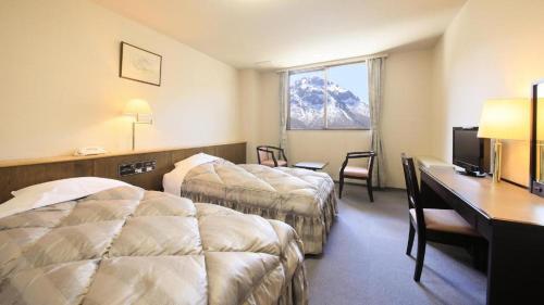 a hotel room with two beds and a desk at Kamikochi Taishoike Hotel in Matsumoto