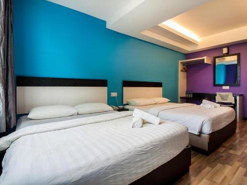 two beds in a room with a blue wall at e Hotel in Melaka