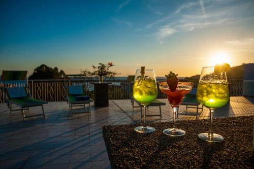 three wine glasses sitting on a table with the sunset at Hotel La Carruba in Cetraro