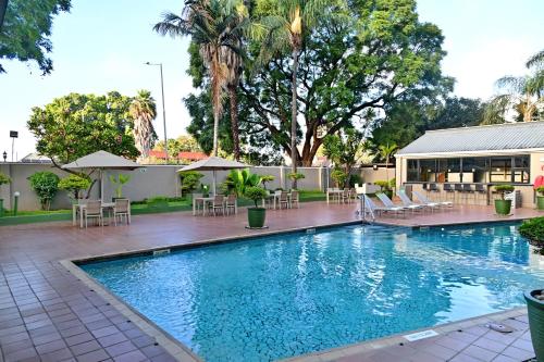 a swimming pool with chairs and tables and a building at Holiday Inn - Harare by IHG in Harare