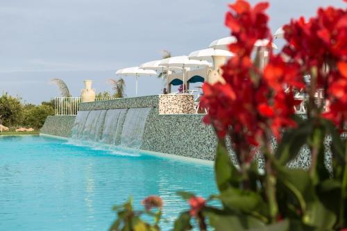 a swimming pool with red flowers in the foreground at Wellness Spa Hotel Principe Fitalia in Siracusa
