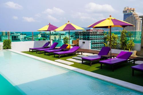 a rooftop pool with purple lounge chairs and umbrellas at The AIM Patong Hotel in Patong Beach