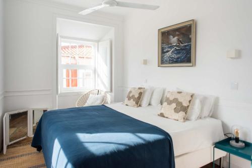 a white bedroom with a bed with a blue blanket at Central Ericeira Apartment with Lift in Ericeira