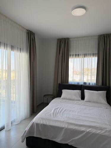 a bedroom with a bed with white sheets and windows at ΘΕΑ 5 Comfortable 1BR and 2BR Apartments in Mor Menekshe