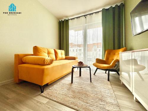 a living room with an orange couch and a chair at Pod Brzozami Apartamenty Let's Sea Gąski in Gąski