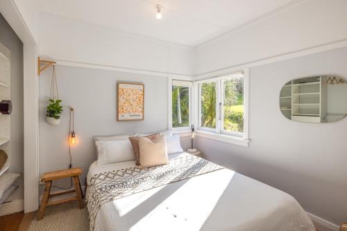 ein weißes Schlafzimmer mit einem Bett und zwei Fenstern in der Unterkunft Hideaway Cottage in Oneroa
