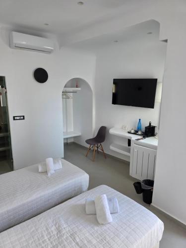 a room with two beds and a desk and a tv at Tataki Family Hotel in Fira