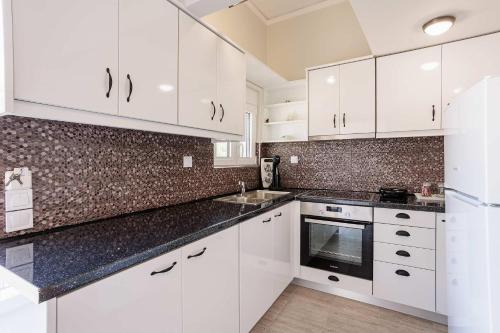 a kitchen with white cabinets and a black counter top at Seaview and Sunsets - Beachside Retreats in Ayía Kiriakí