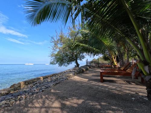 a bench sitting next to the ocean with palm trees at Maryan Moyo Bungalows & Resto in Moyo Island