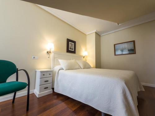 a bedroom with a white bed and a green chair at Apartamentos Verdemar (VUT) in Llanes