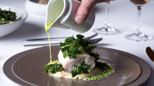a person drizzling sauce on a plate of food at Mitsis N'U Piraeus Port in Piraeus