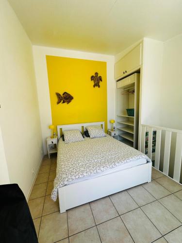 une chambre avec un lit blanc et un mur jaune dans l'établissement La Marine' Hyères, à Hyères