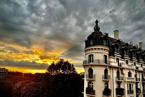 un grand bâtiment blanc avec un coucher de soleil en arrière-plan dans l'établissement Appart Hôtel - Vue unique, à Vichy