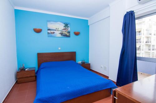 Dormitorio azul con cama y ventana en Akisol Armação Pera Beach IV, en Armação de Pêra