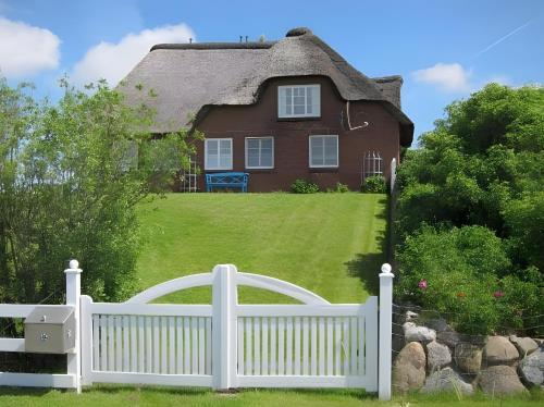 a white fence in front of a thatched house at Ferienhaus Tammwarfthuus in Pellworm