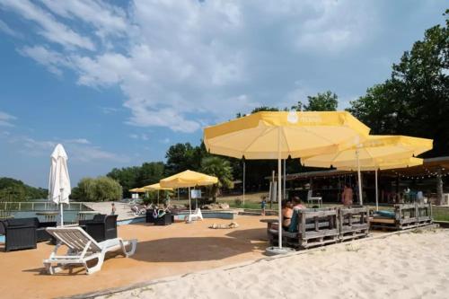 a patio with chairs and umbrellas on a beach at Chalets Camping Lacs d'Armagnac in Bretagne-dʼArmagnac