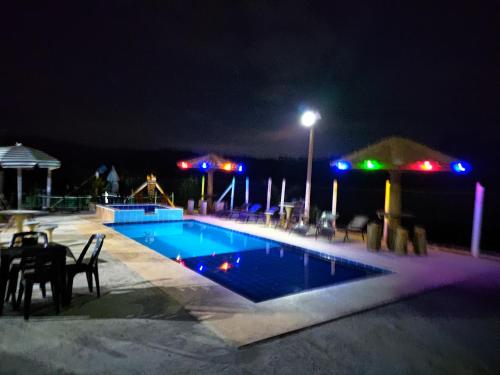 a swimming pool at night with a table and chairs at Pousada irmãos Oliveira in Lindóia