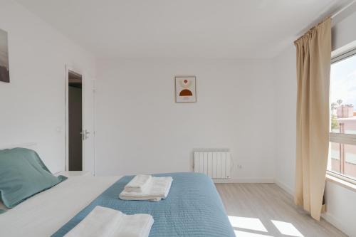 a white bedroom with a blue bed and a window at Bright & Family Flat in Paço de Arcos by HostWise in Lisbon