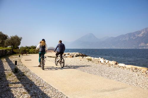 a man and woman riding bikes on a path by the water at Sunset Residence in Brenzone sul Garda