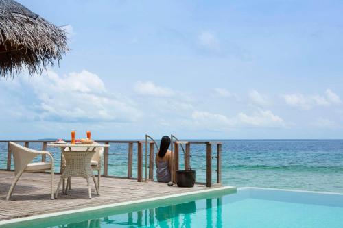 a woman sitting at a table next to the ocean at Dusit Thani Maldives - 50 percent discount on transfers for stays until 20 Dec 2025 in Baa Atoll