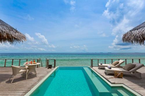 a swimming pool with chairs and a table and the ocean at Dusit Thani Maldives - 50 percent discount on transfers for stays until 20 Dec 2025 in Baa Atoll