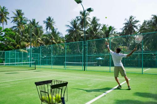 a man serving a tennis ball on a tennis court at Dusit Thani Maldives - 50 percent discount on transfers for stays until 20 Dec 2025 in Baa Atoll