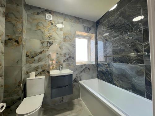 a bathroom with a tub and a toilet and a sink at Brand New, Immaculate 3 Bed 3 Shower room House in Cheshunt