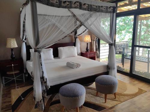 a bedroom with a canopy bed with two ottomans at Living Waters Resort in Jinja