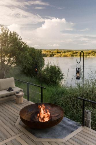 a fire pit on a deck next to a river at Zambezi Sands by Batoka in Victoria Falls