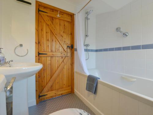La salle de bains est pourvue d'une porte en bois, d'une baignoire et d'un lavabo. dans l'établissement Lavender Cottage, à Okehampton