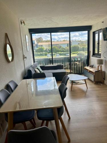 - un salon avec une table, des chaises et une grande fenêtre dans l'établissement Le Wharf, à Seignosse