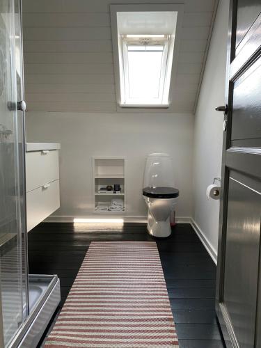 a bathroom with a toilet with a window and a rug at Cozy big apartment in Blokhus