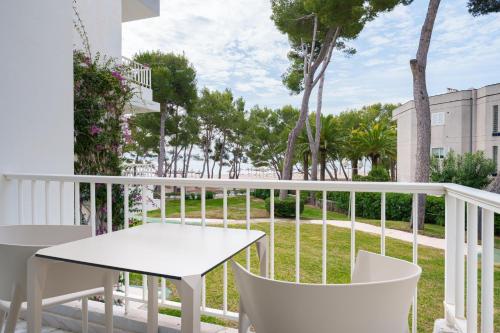 a white table and chairs on a balcony with trees at Apartamentos Caprice Playa de Alcudia in Port d'Alcudia