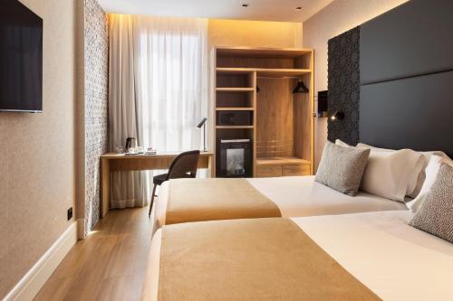 a hotel room with two beds and a desk at Catalonia Giralda in Seville