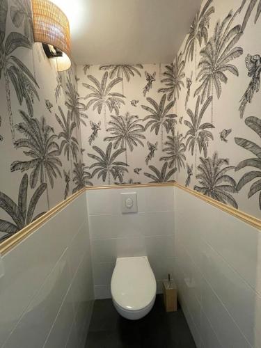 une salle de bain avec toilettes et papier peint palmiers dans l'établissement Bienvenue à la maison, à Saint-Florentin