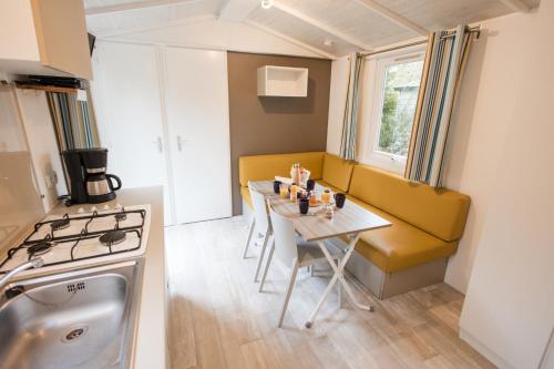 une petite cuisine avec une table et un canapé jaune dans l'établissement Camping les Chelles, à Olliergues