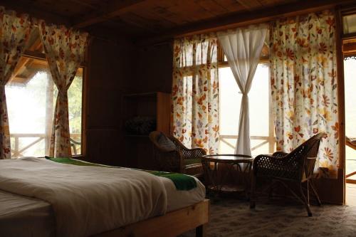a bedroom with a bed and two chairs and windows at Mountain Mamma in Shangarh