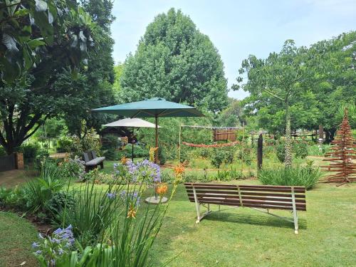 a park bench with an umbrella in a garden at Windsong Living The Nest in Krugersdorp