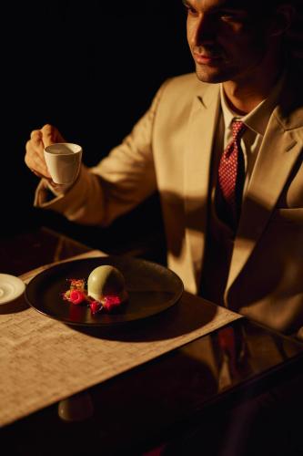a man in a suit holding a cup and a plate of food at Royal Maxim Palace Kempinski Cairo in Cairo