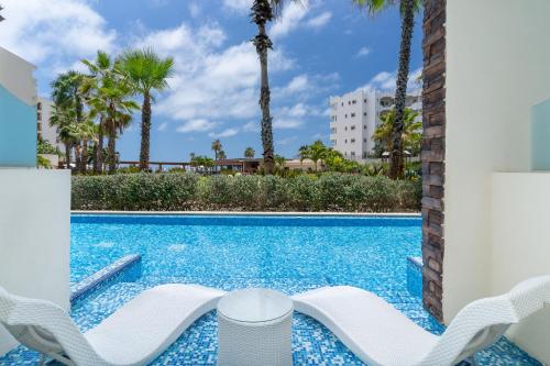 a swimming pool with two lounge chairs and palm trees at Krystal Grand Los Cabos - All Inclusive in San José del Cabo