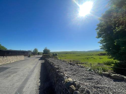 a road with a stone wall and the sun in the sky at Lake District Stunning Lodge in Plumbland