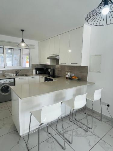 a kitchen with white cabinets and a counter with white chairs at Sea Breeze - Oroklini in Voroklini